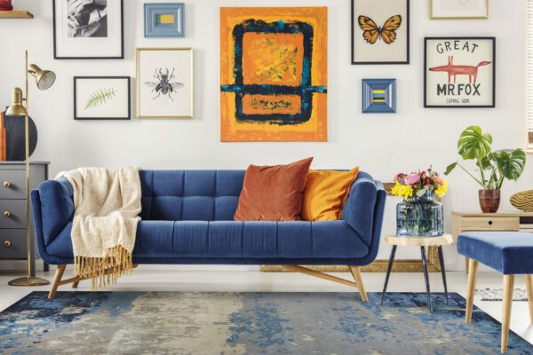 Painting above navy blue couch in artistic living room interior with colorful rug. Real photo