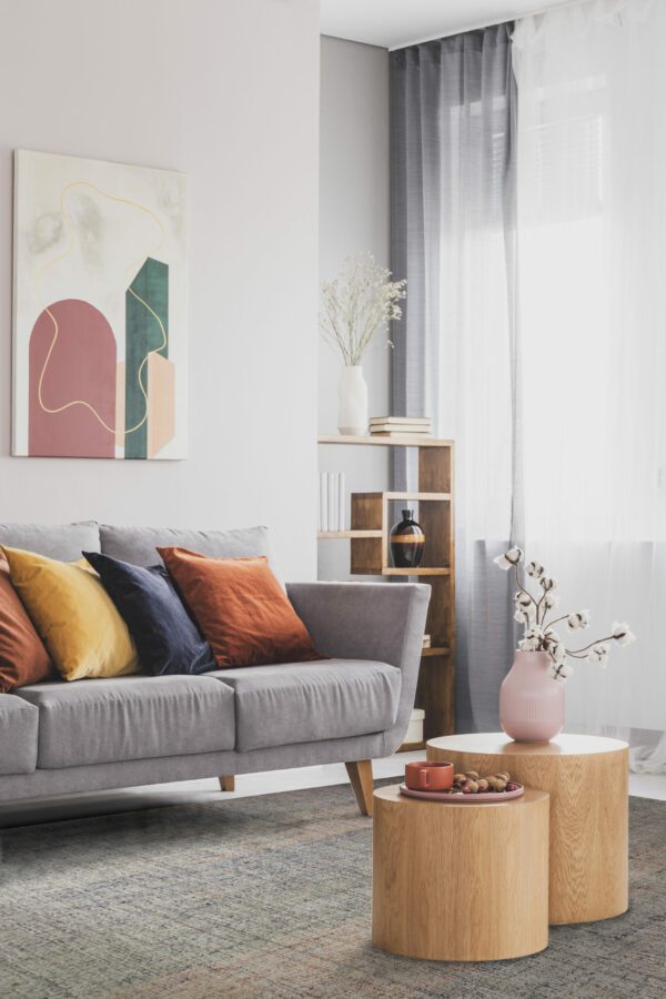 Flowers in pastel pink vase on wooden coffee table in front of grey scandinavian couch with colorful pillows