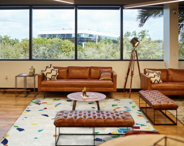 Wide angle view of modern office lobby with brown leather seating, rugs, tables, and expansive view.