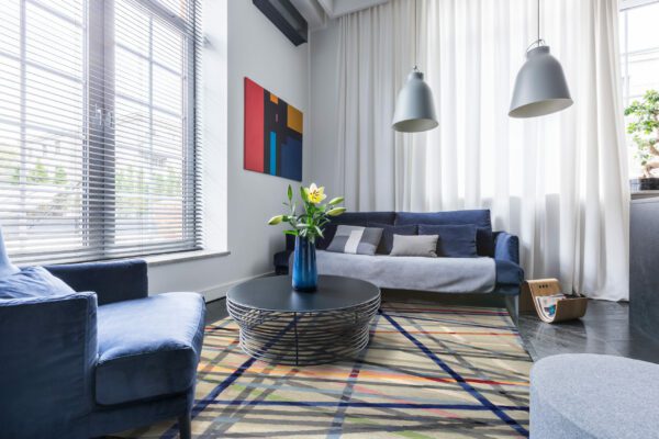 Living room with blue upholstered furniture, window blinds and white net curtain