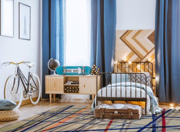 Teenager's bedroom interior with blue bicycle and skateboard on a wooden cupboard next to the bed