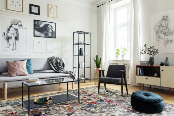 Pouf next to armchair in living room interior with table in front of sofa under posters. Real photo