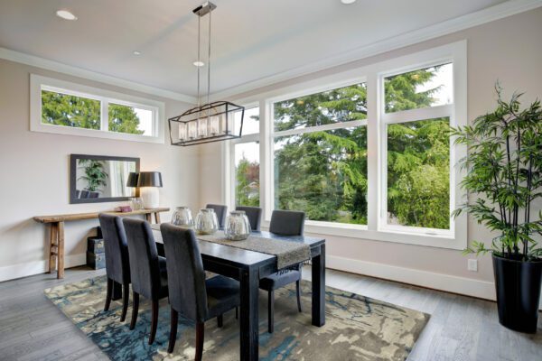 Luxurious modern dining room boasts a black dining table illuminated by a rectangular chandelier and surrounded by gray velvet dining chairs over taupe sisal rug finished with rustic console table.