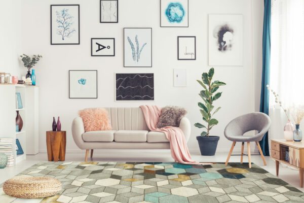 Pouf on blue carpet in spacious pink living room interior with grey armchair next to sofa and ficus