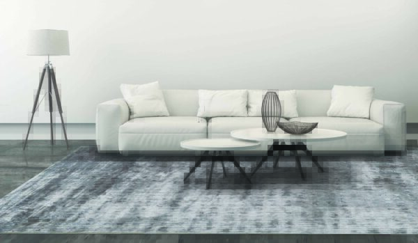 White sofa with set of coffee tables, a floor lamp and pillows. Interior is white, brightly lit with ornate carpet. Concrete industrial floor and a white wall behing. Copy space. 3D render